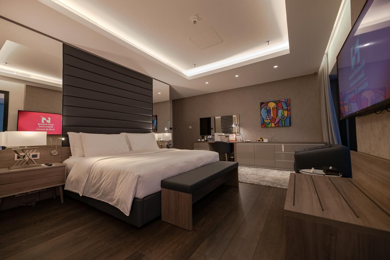 Moderna camera d'albergo con letto king size, panca, scrivania, TV e opere d'arte alle pareti.