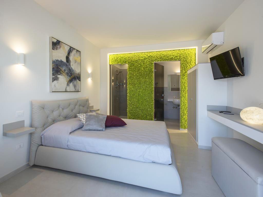 Camera da letto con pareti bianche, un letto grigio e una parete di muschio che conduce al bagno.