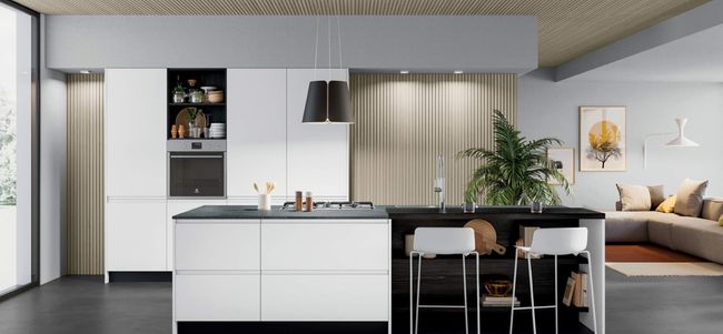 Cucina moderna con mobili bianchi, isola nera e sedute. Colori neutri con un tocco di verde e arte.