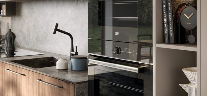 Cucina moderna con mobili in legno, lavello scuro, rubinetto nero e forno. Mensole con libri e orologio.