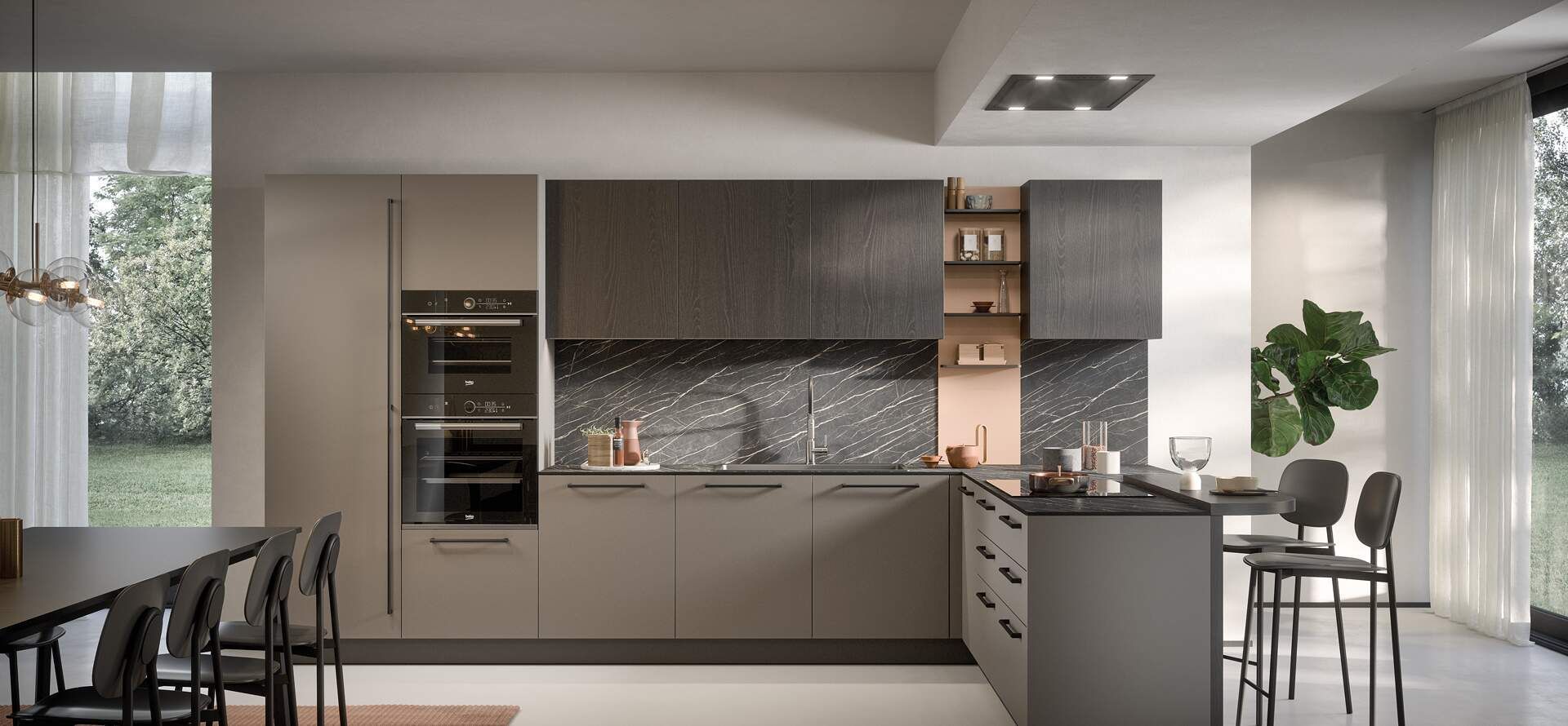 Cucina moderna con mobili grigi, piano di lavoro scuro e isola con sedute. Ampie finestre lasciano entrare la luce naturale.