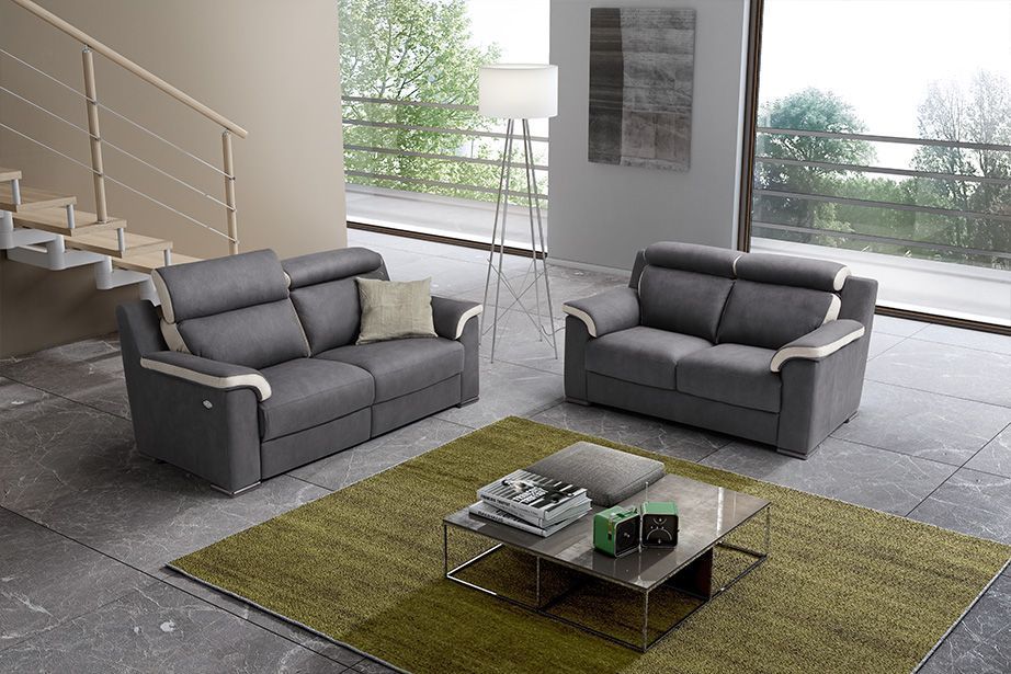 Divano grigio in un soggiorno moderno con tappeto verde, tavolino e scala.