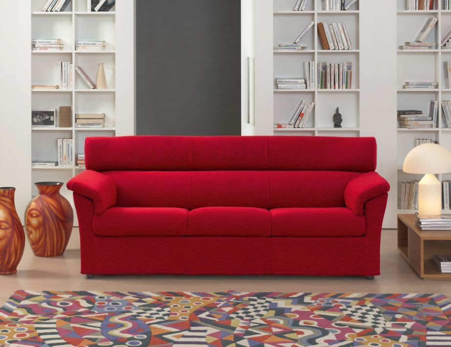 Divano rosso in un soggiorno moderno, affiancato da vasi e una libreria.