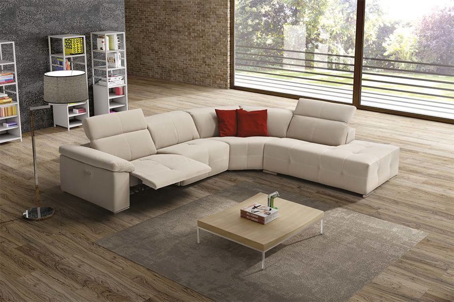 Divano componibile beige con elementi reclinabili, cuscini rossi e tavolino da caffè in un soggiorno moderno.