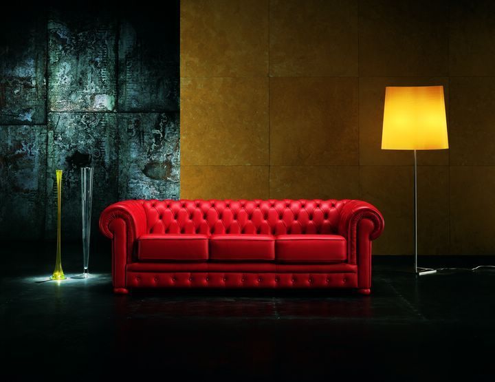 Divano in pelle rossa trapuntata contro una parete scura e dorata. Lampada e vasi sulla sinistra.