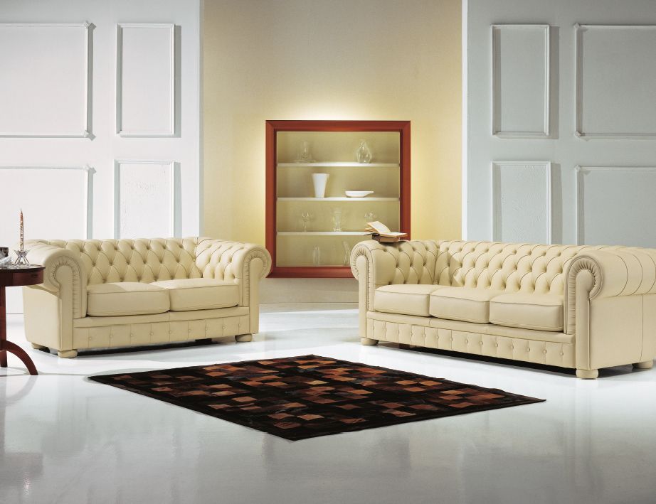 Due divani beige con bottoni sono uno di fronte all'altro, con una vetrina, un tappeto e un tavolino laterale.