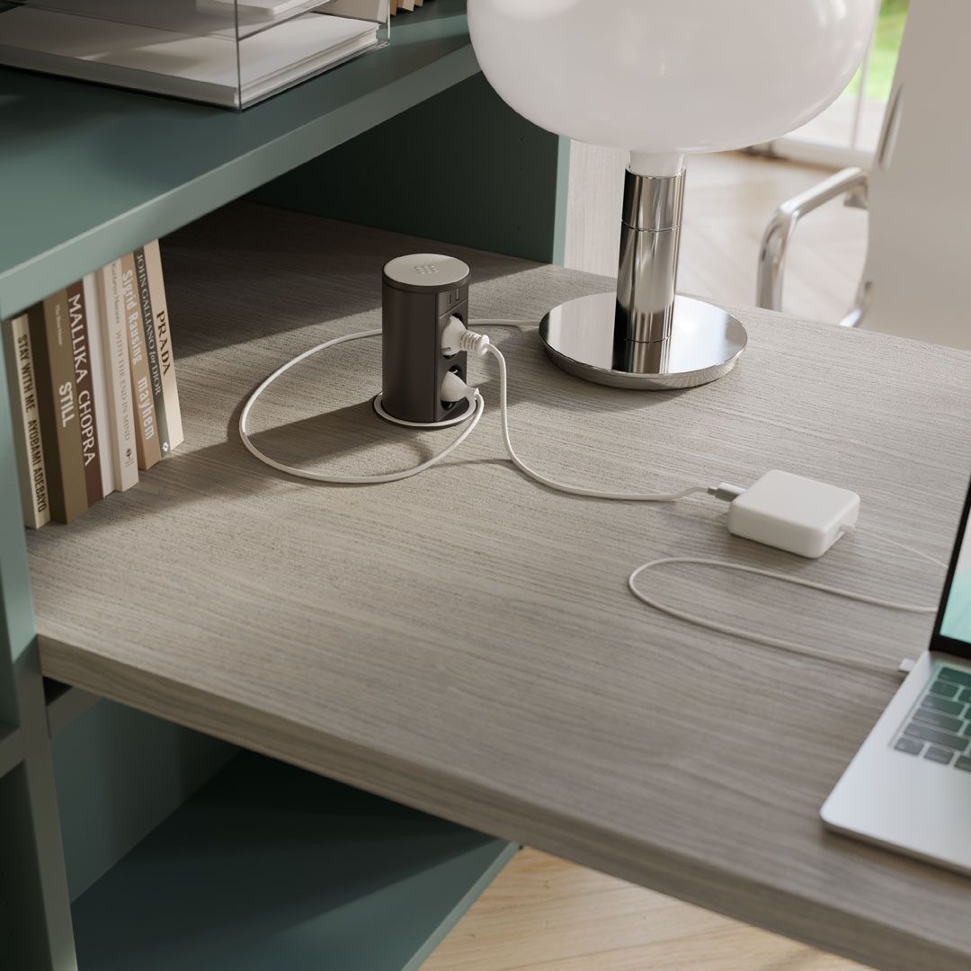 Scrivania con libri, lampada, hub di ricarica e computer portatile. Superficie in legno grigio e ripiani color verde acqua.