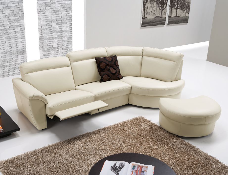 Divano componibile color crema con poltrona reclinabile e pouf su un tappeto marrone, in una stanza bianca.