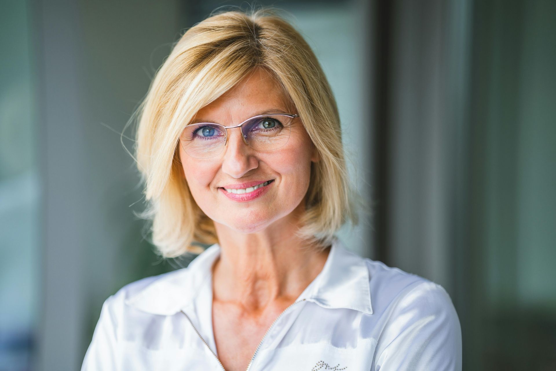 A woman wearing glasses and a white shirt is smiling for the camera.