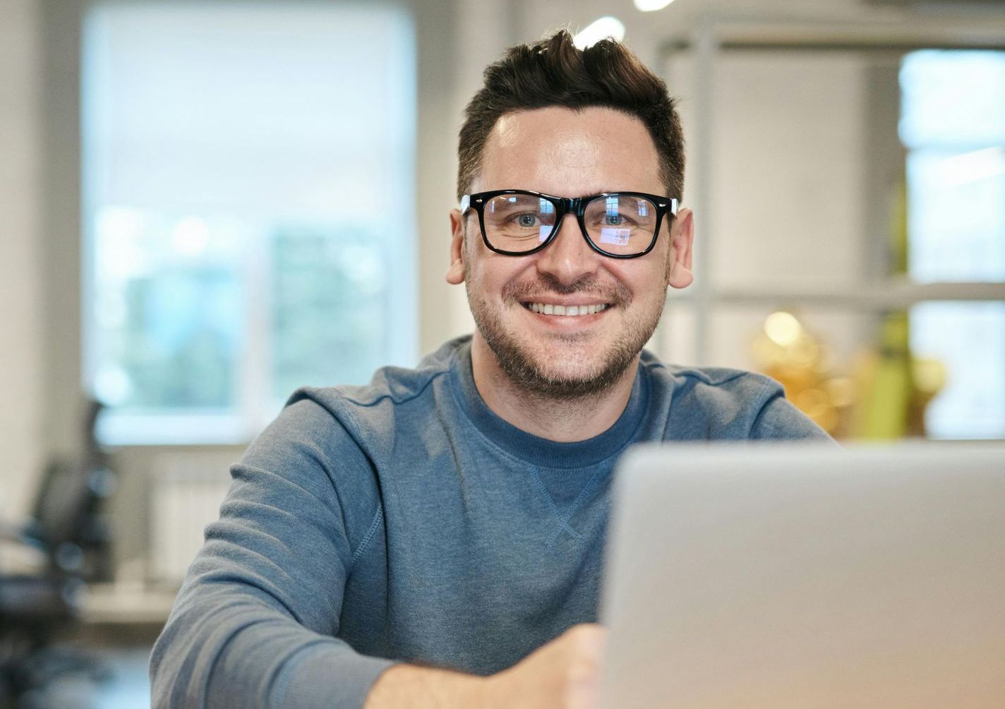 A man wearing glasses is sitting in front of a laptop computer.