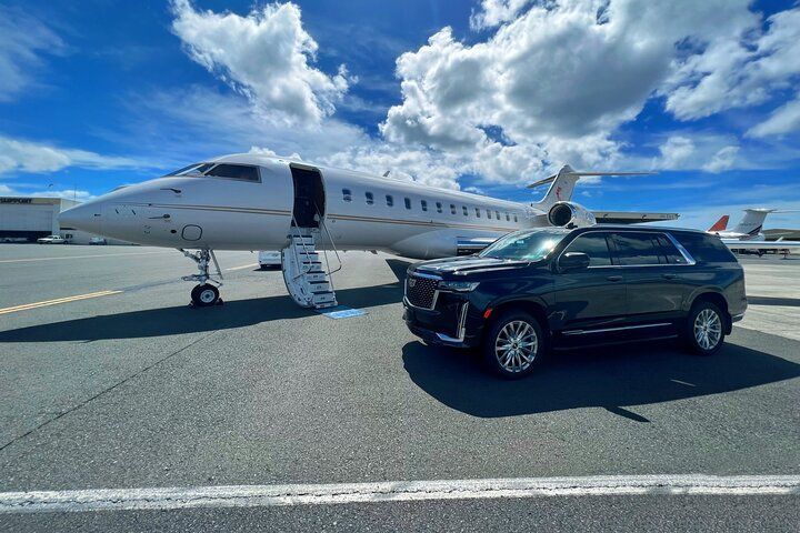 A car is parked next to a private jet at an airport.