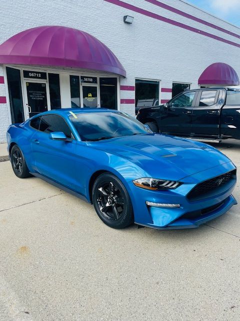 Blue Ford Mustang parked in front of a building with purple awnings.