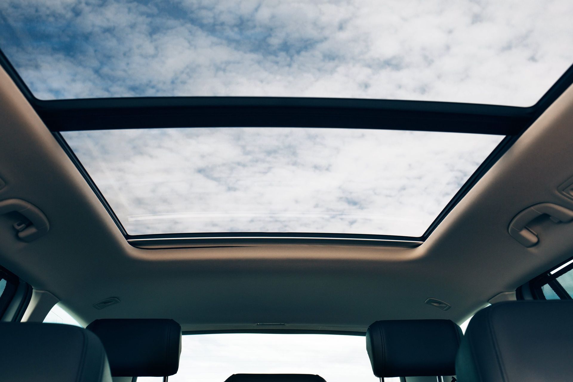 Interior view of a car with open sunroof, showing blue sky and clouds.