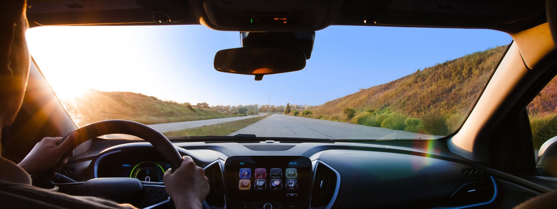View from inside a car, driving on a sunny road with mountains in the distance.