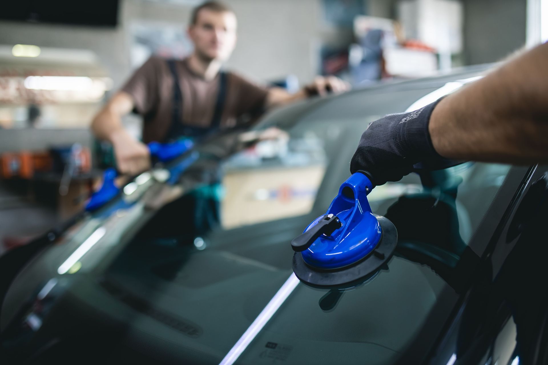 Two auto technicians using suction cups to install a windshield in a repair shop.