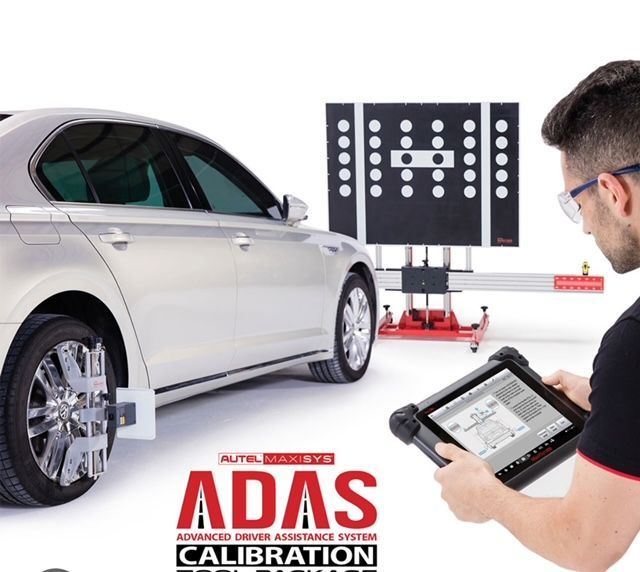 Man calibrates car's advanced driver assistance system (ADAS). Silver car, alignment machine, tablet. White background.
