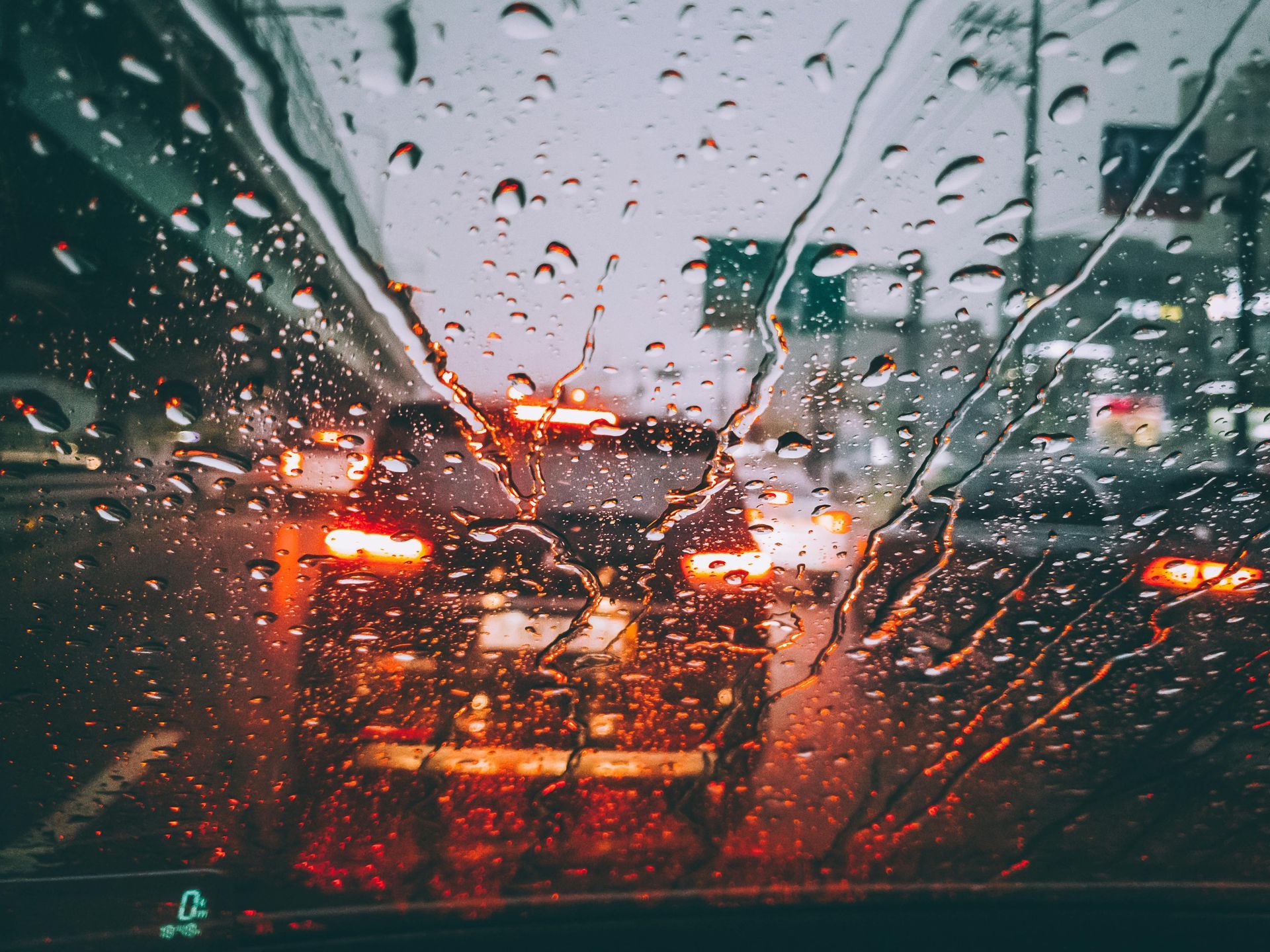 Raindrops on a car windshield blur traffic lights, creating a hazy, orange and gray scene.