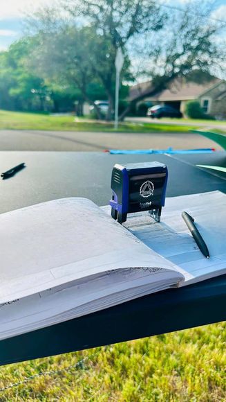 A purple stamp is sitting on top of a notebook with a pen.