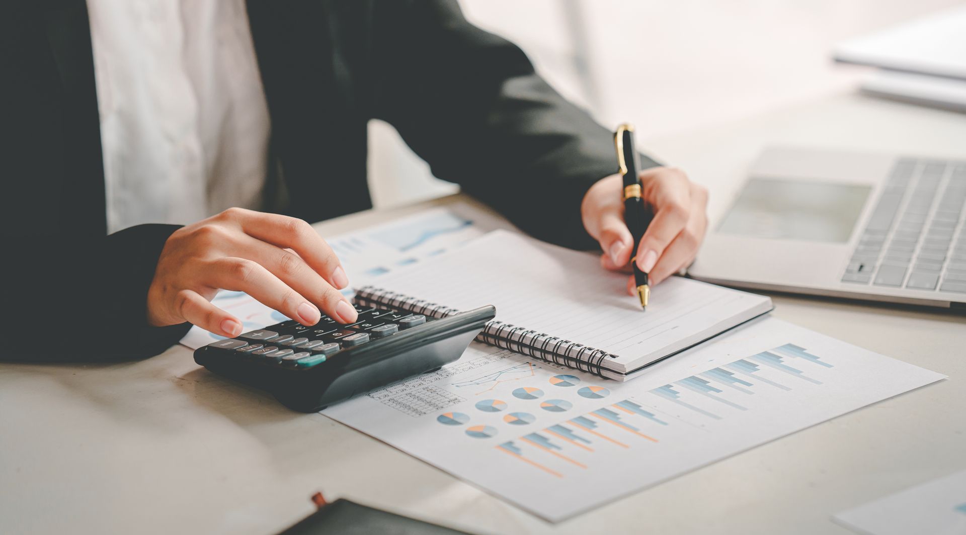 A woman is sitting at a desk using a calculator and writing in a notebook.