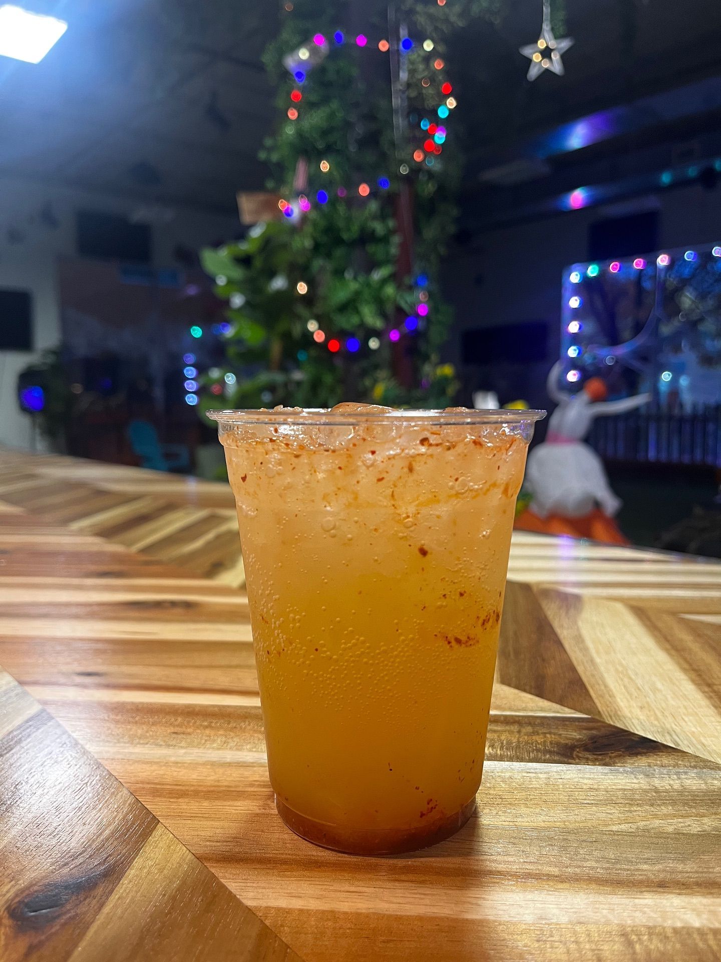 Glass of yellow cocktail with chili rim on wooden bar, Christmas tree in the background.