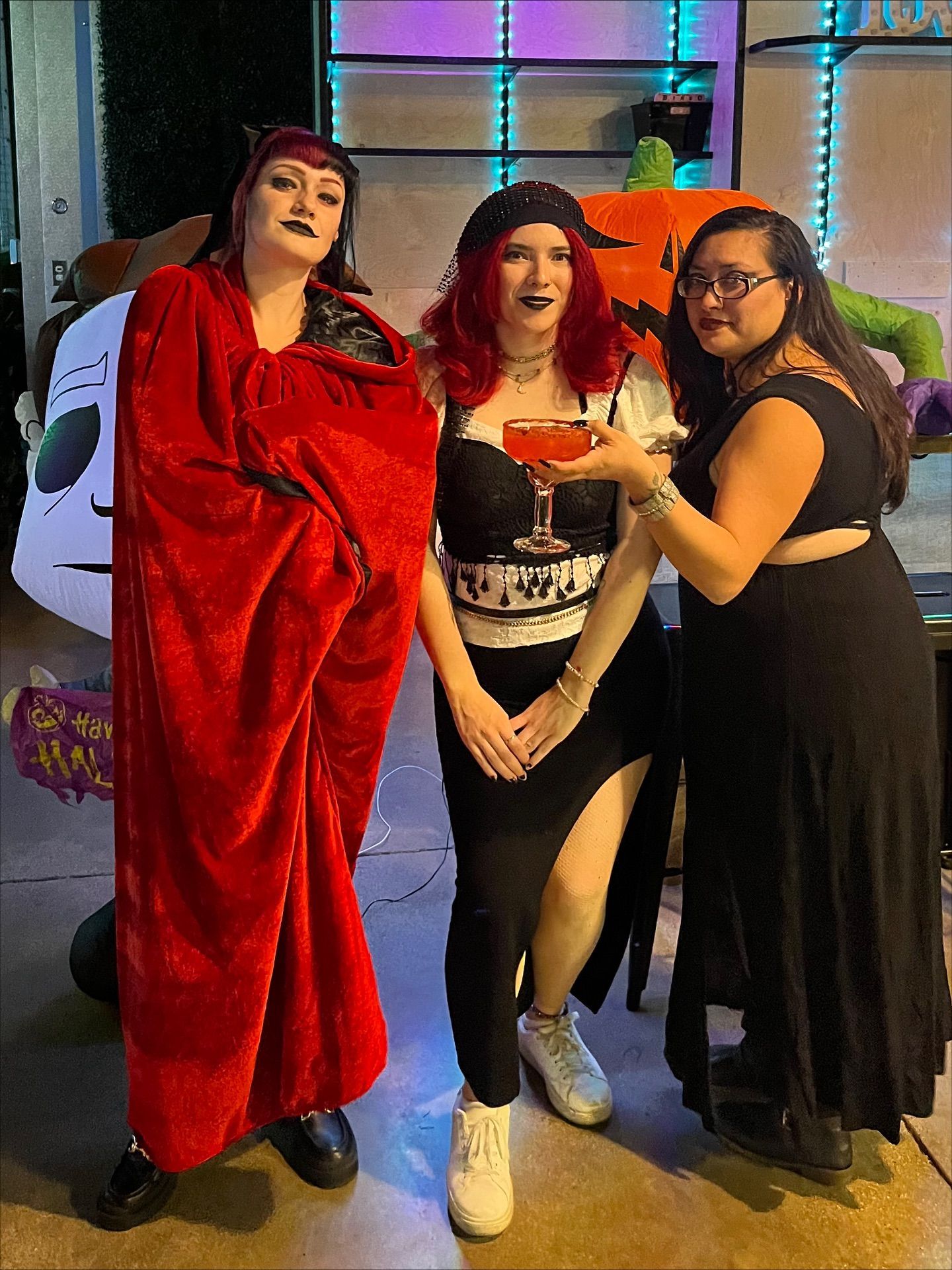 Three people in Halloween costumes posing outdoors with festive decorations.