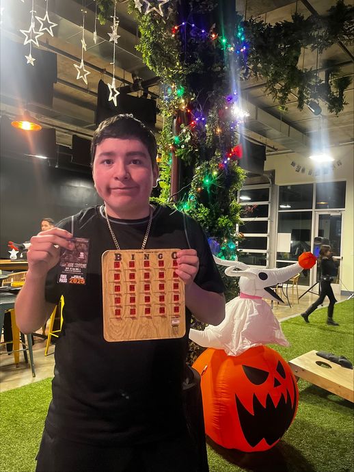 Person holding game pieces, smiling. Beside an inflatable Zero from The Nightmare Before Christmas and a decorated tree.