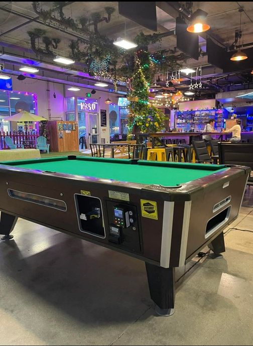 Pool table in a bar setting, with a Christmas tree and bar in the background.