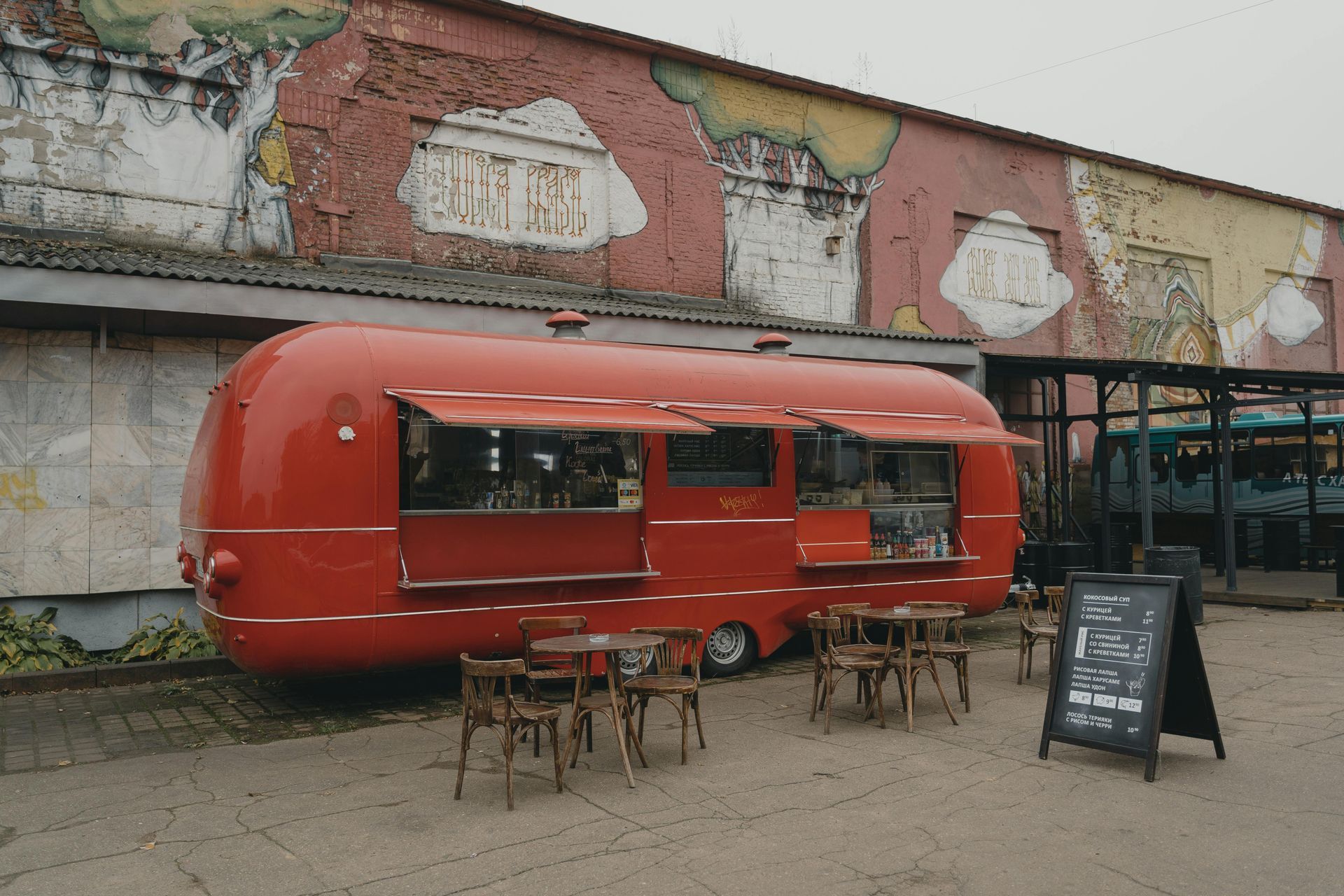 Red food truck with open windows, outdoor seating, and menu board.