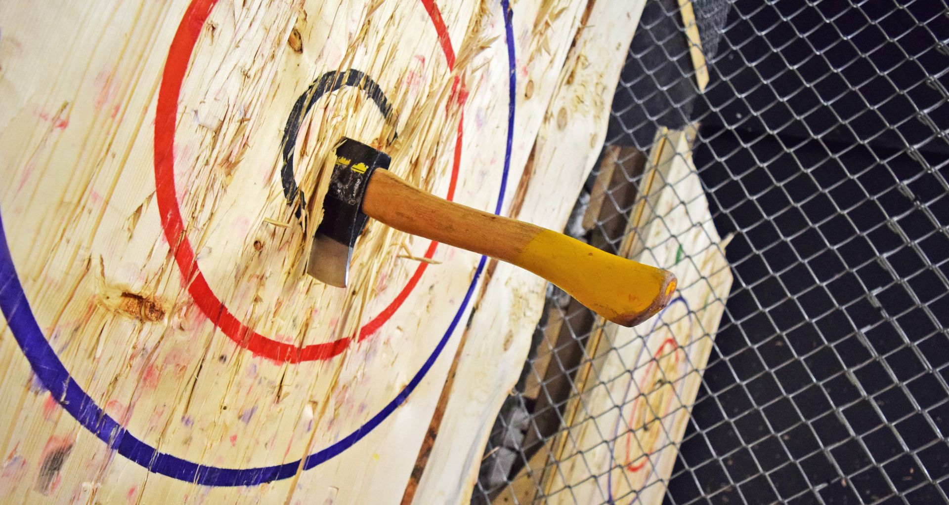 Axe embedded in a wooden target with red, blue, and black concentric circles.