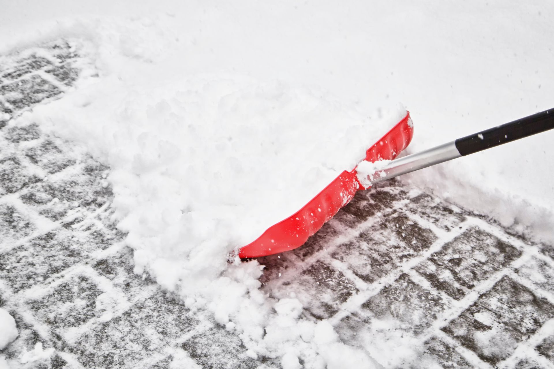 Red snow shovel clearing snow from a paved walkway