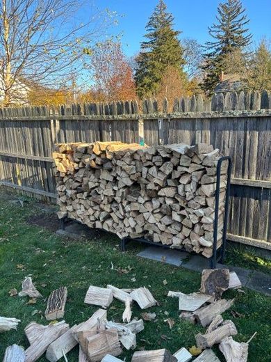 Gloved hands holding split firewood logs against a stacked woodpile background