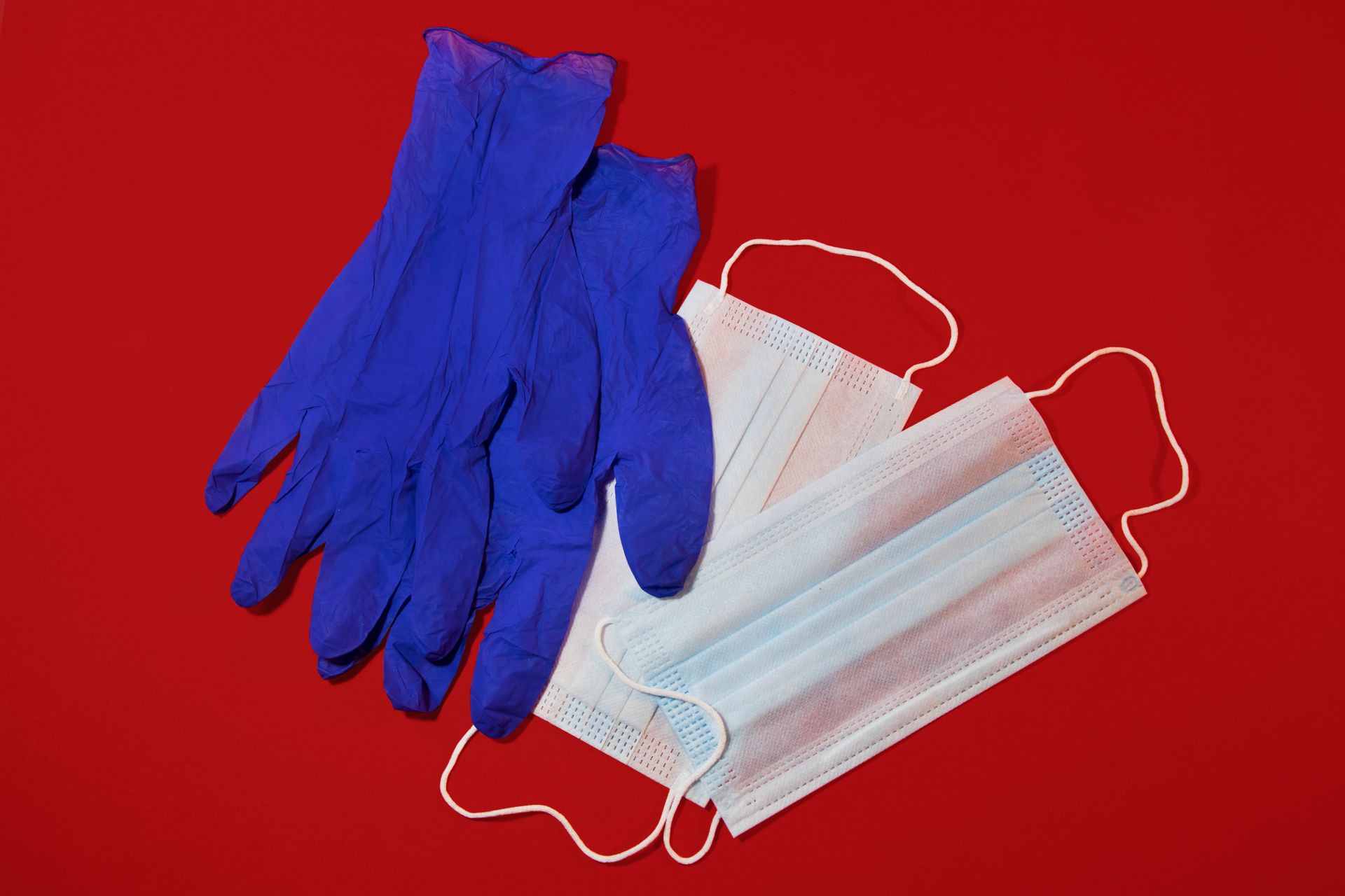 A pair of blue gloves and three face masks on a red surface.