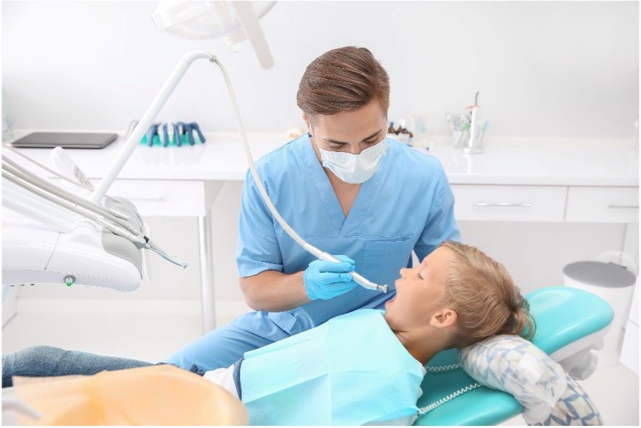 A young boy is sitting in a dental chair getting his teeth examined by a dentist wearing nitrile gloves.