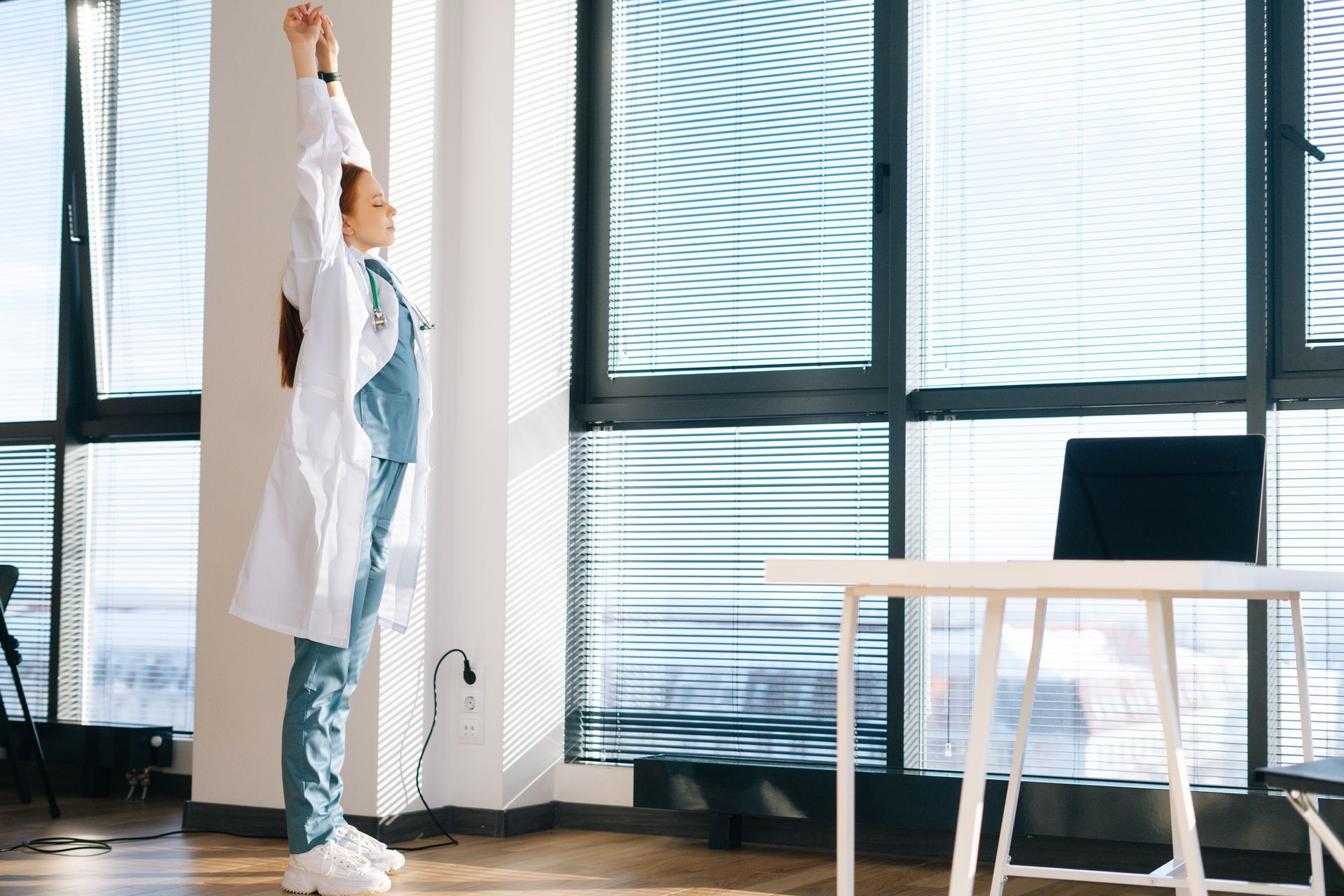 A female doctor is stretching her arms in an office to encourage her mental health.