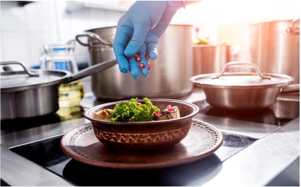 A person is adding pomegranate to a bowl of salad with blue latex gloves.