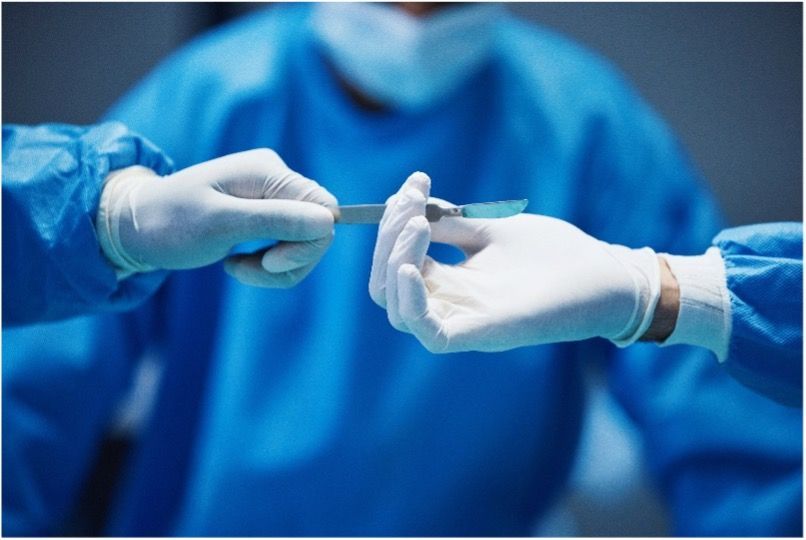 A surgeon is giving a scalpel to another surgeon with white latex gloves on.