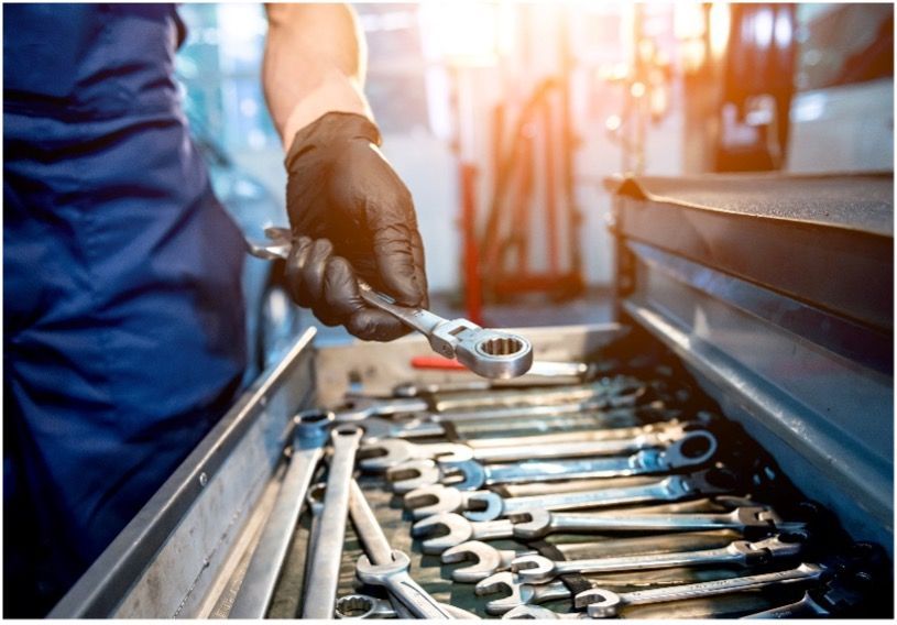 A man is holding a wrench over a tray of wrenches with black nitrile gloves on.