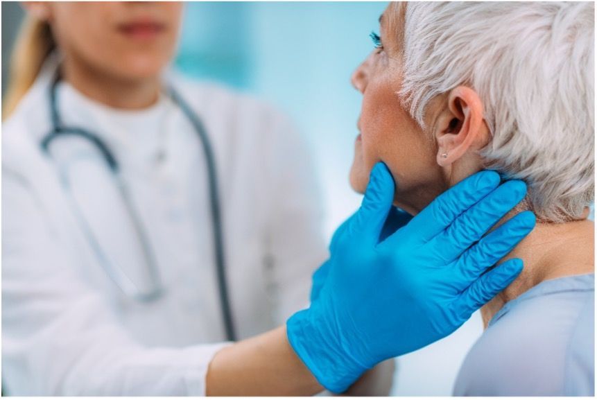 A doctor while wearing latex gloves is assessing a patient's neck.