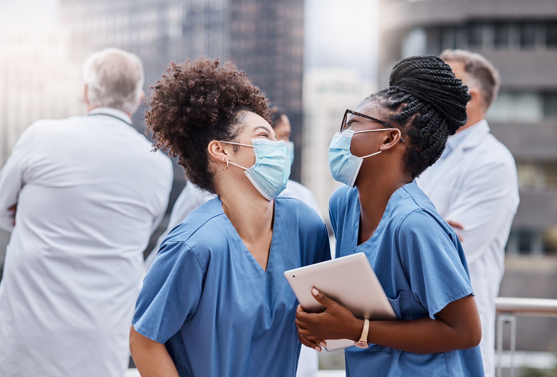 Two nurses wearing face masks are looking at each other.