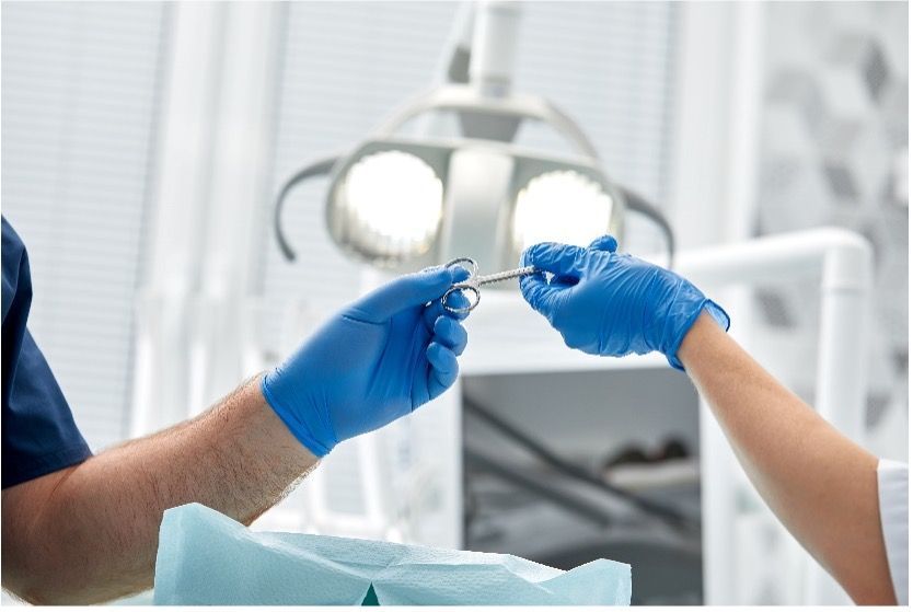 A dentist is holding a pair of scissors over his assistant while both are wearing blue gloves.