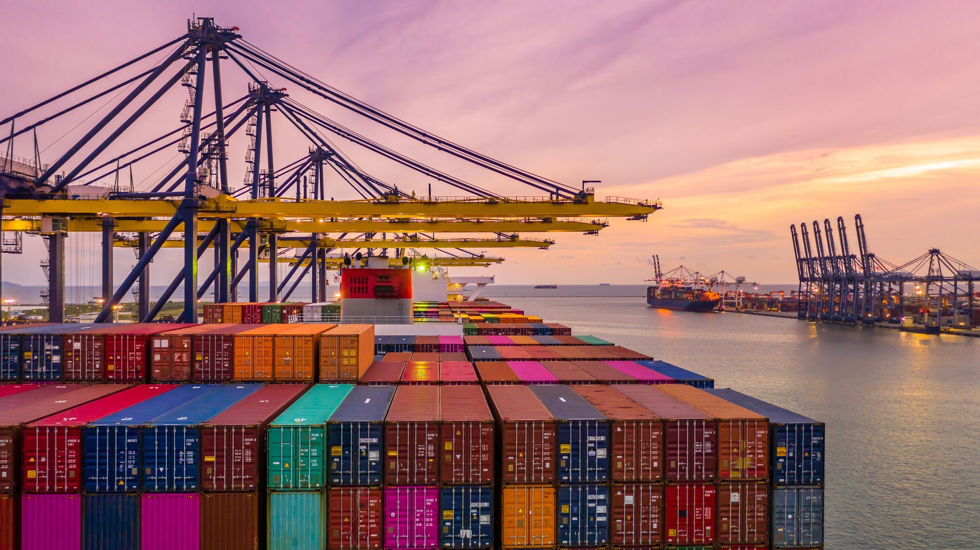 A large container ship is docked in a harbor at sunset.