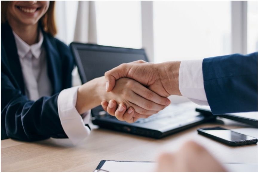 A man and a woman are shaking hands over a table during a meeting about supply chain operations.