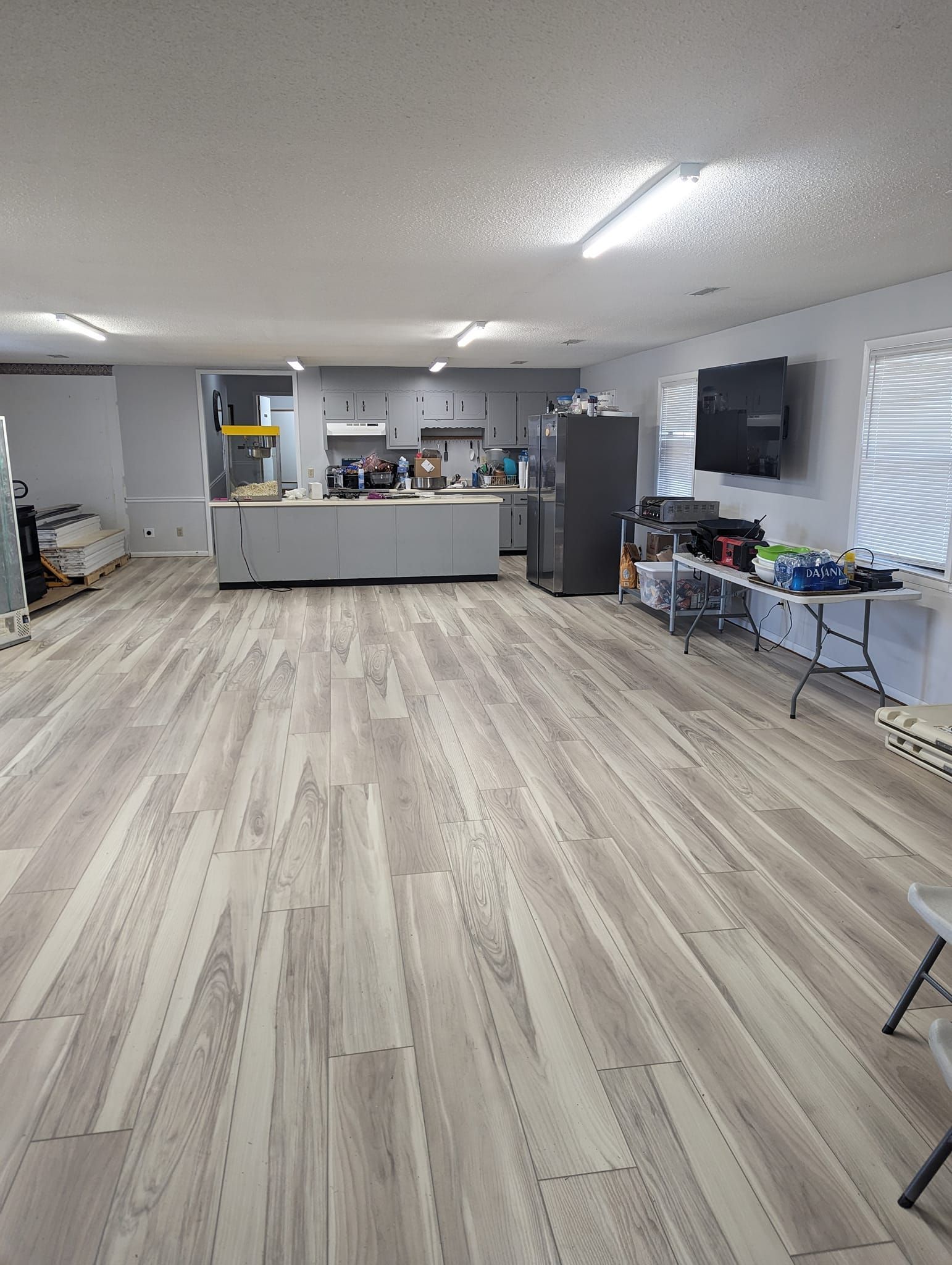 A large room with a wooden floor and a kitchen in the background.