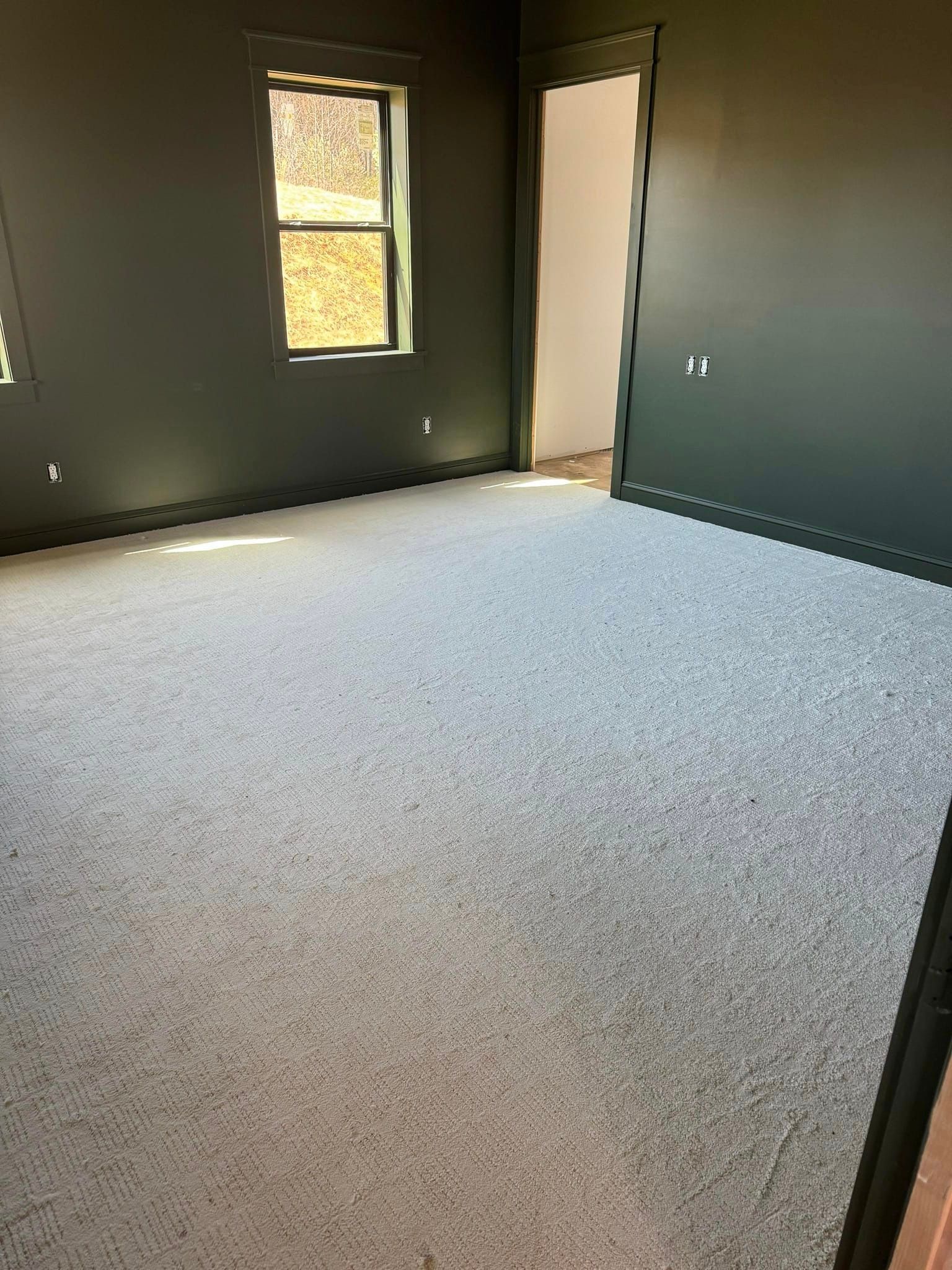 An empty room with a carpeted floor and a window.