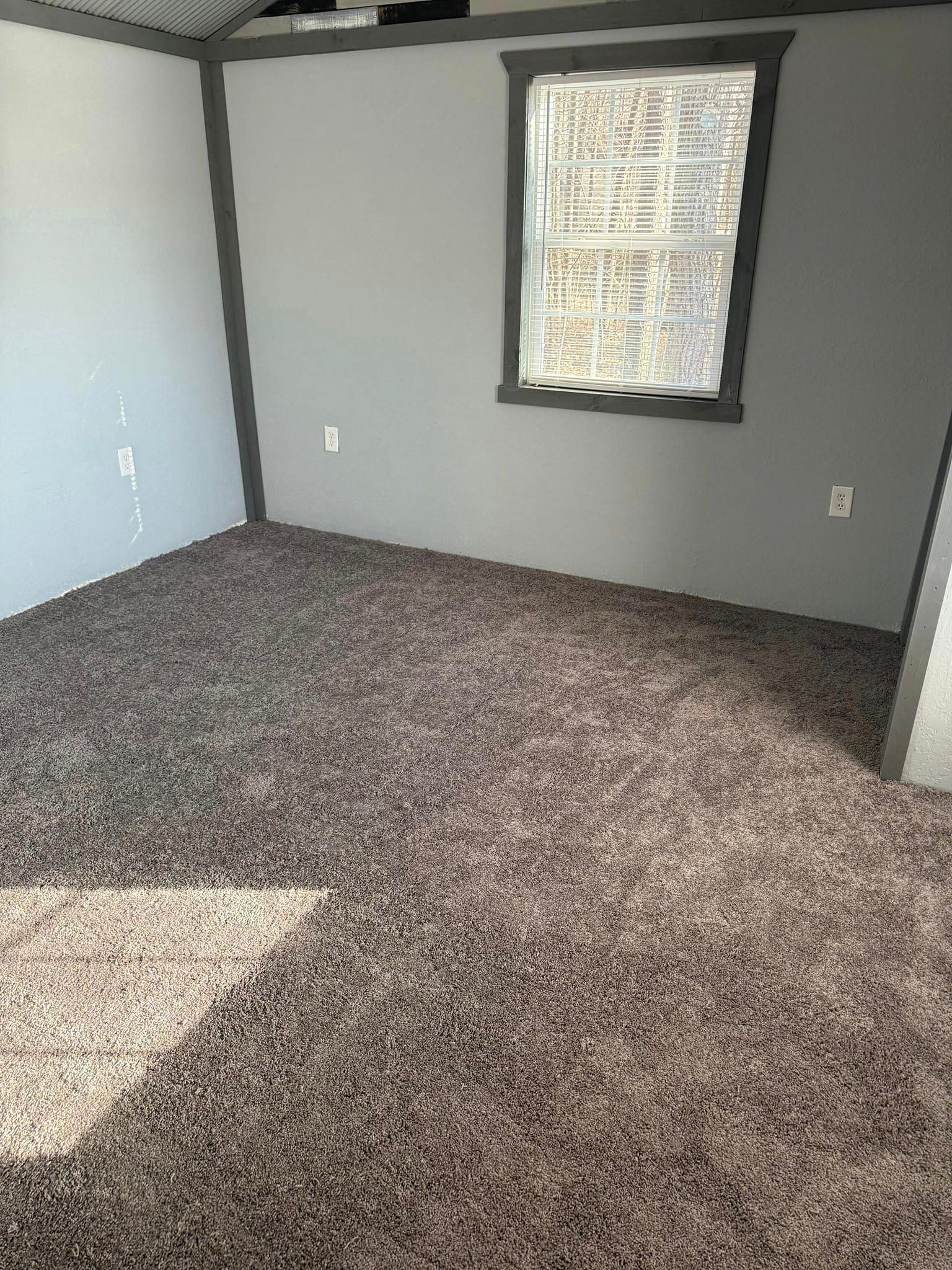 An empty room with a carpeted floor and a window.
