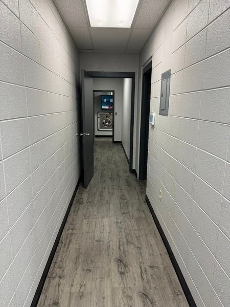 A long hallway with white brick walls and wooden floors leading to a door.