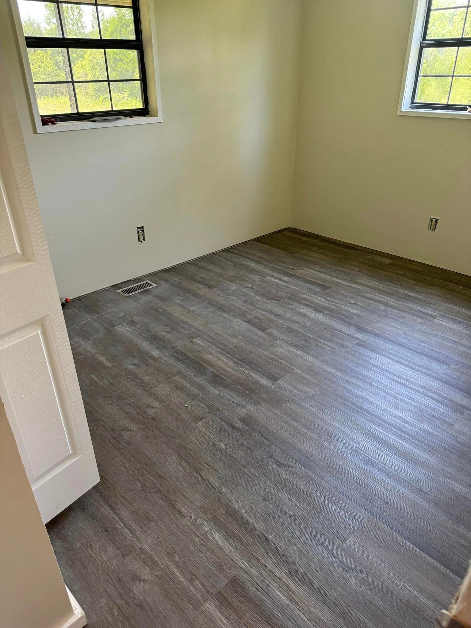 A room with a wooden floor and two windows.