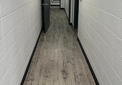 A long hallway with a wooden floor and white brick walls.