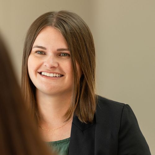 A woman in a black jacket is smiling and looking at the camera.