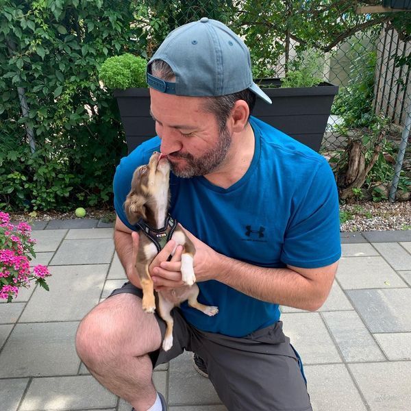 Man kneels kissing small puppy outdoors